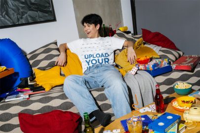 Comfort Colors Tee Mockup Featuring a Happy Man on a Couch Surrounded by Games and Junk Food