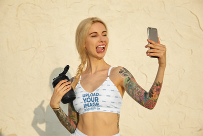 Sports Bra Mockup of a Tattooed Woman Taking a Selfie with Her Tongue Out