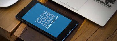 Mockup of a Black Nexus 7 in Portrait Mode by a Laptop