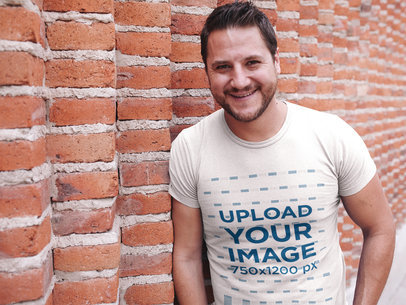 Smiling Dude Wearing a Tshirt Mockup While Lying Against a Bricks Wall