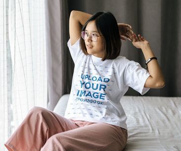 Unisex T-Shirt Mockup Featuring a Young Woman Sitting on a Bed