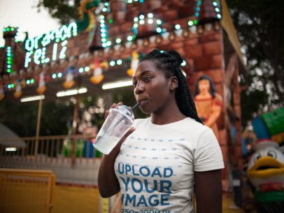 Girl Drinking a Cold Beverage While Wearing a Tshirt Mockup at an Amusement Park a15961