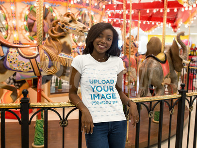 Mockup of a Young Woman Wearing a T-shirt  While Happily Standing Against a Carousel