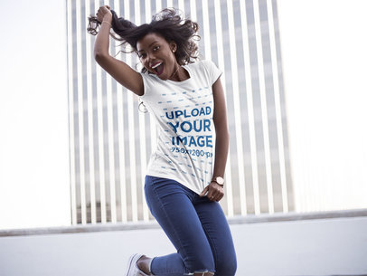 Mockup of a Young Woman Wearing a T-Shirt While Jumping and Smiling Against a Building 16047