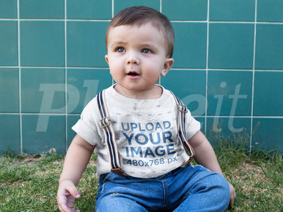 Little Baby Boy Wearing a Round Neck Tee Mockup While Sitting Down in the Grass
