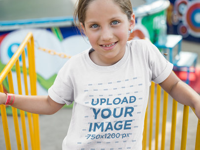 Little Smiling Girl Wearing a T-Shirt Mockup While waiting on an Amusement Park Line