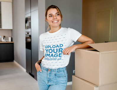 T-Shirt Mockup of a Smiling Woman Standing Next to Moving Boxes at Home