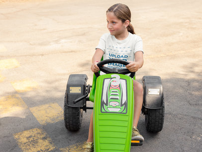 Mockup of a Young Girl Wearing a T-Shirt Mockup While Driving a Green Plastic Go Kart