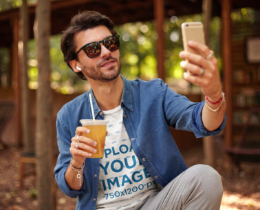 Round-Neck Tee Mockup of a Man with Sunglasses and a Drink Taking a Selfie