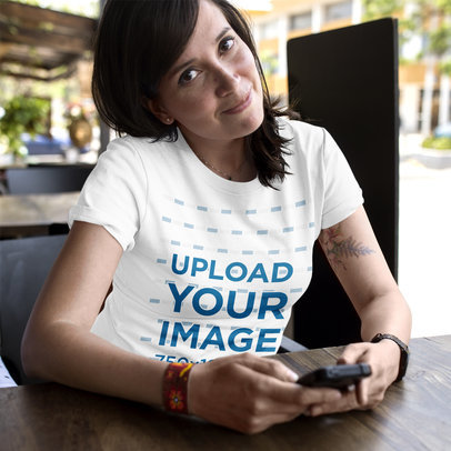 Woman Wearing a T-Shirt Template While at a Coffee Shop Checking her Phone a16189