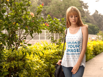 Mockup of a Blonde Woman Wearing a Bella Canvas Tank Top in a Garden