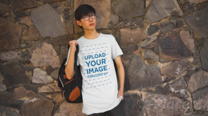 T-Shirt Video of a Young Student with Glasses Posing by a Rock Wall