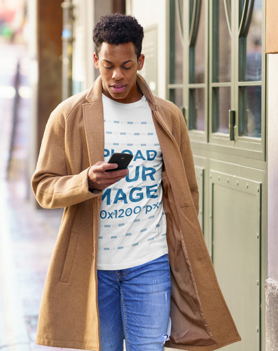 T-Shirt Mockup of a Man Checking His Cellphone and Walking Down the Street