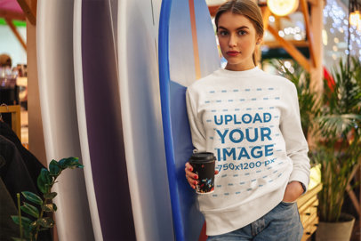 Sweatshirt Mockup of a Woman With a Coffee Cup Leaning Against Surfboards
