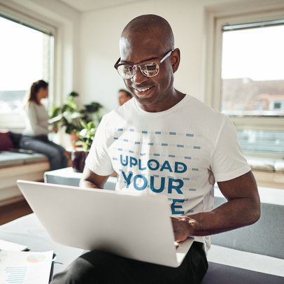 Round-Neck T-Shirt Mockup of a Smiling Man Working on His Laptop