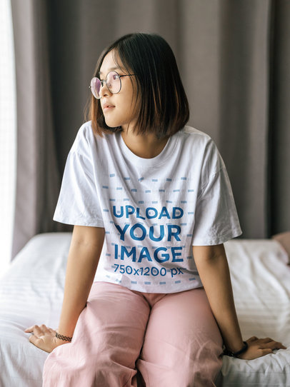 Loose T-Shirt Mockup Featuring a Teenage Girl with Glasses Sitting on Her Bed