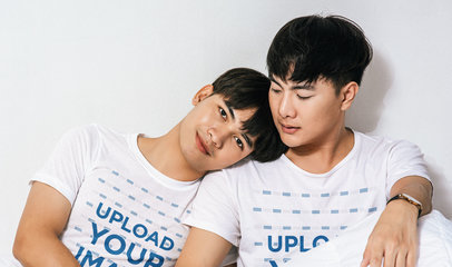 T-Shirt Mockup of Two Men Posing in a Bed With White Sheets