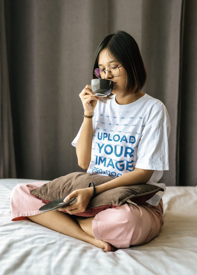 Mockup of a Teenager in a Loose T-Shirt Drinking Coffee on Her Bed