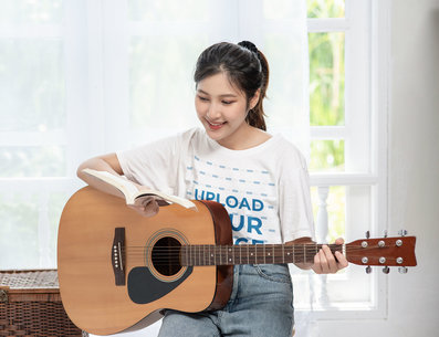 T-Shirt Mockup of a Smiling Woman Playing the Guitar at Home