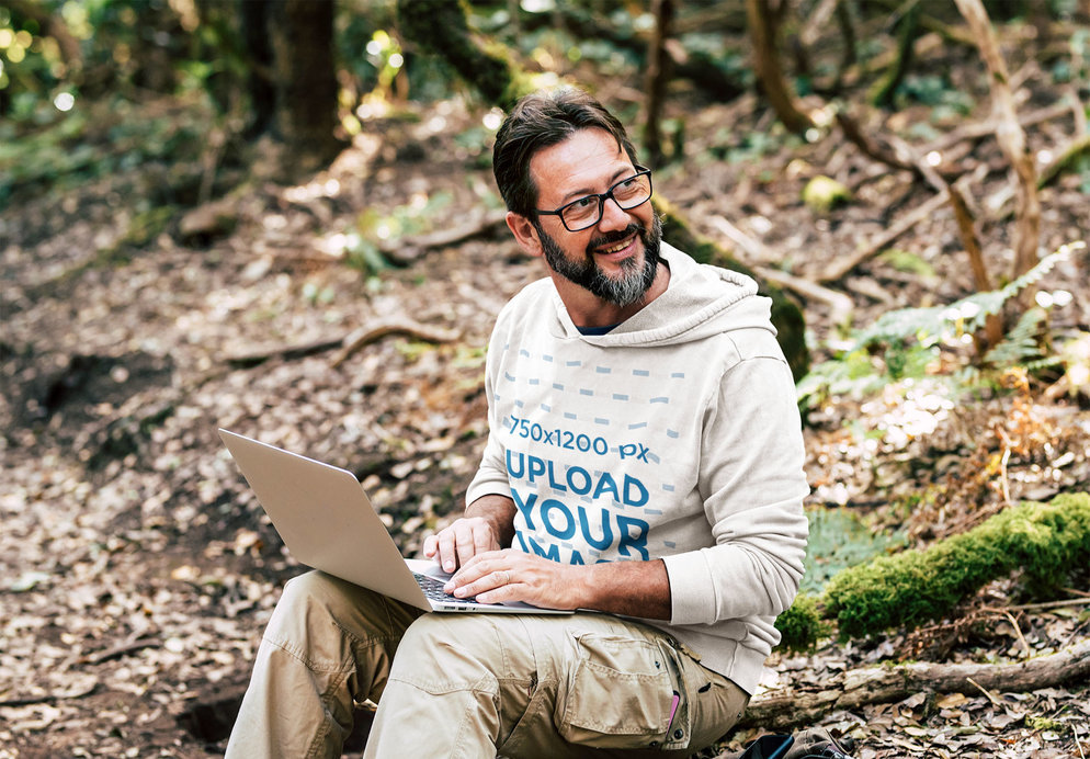 Pullover Hoodie Mockup of a Man in the Woods Working on His Laptop