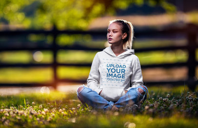 Hoodie Mockup Featuring a Serious Woman Sitting on the Grass