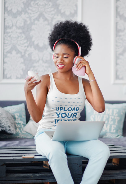 Tank Top Mockup of a Woman Sitting at Home with Headphones and a Computer on Her Lap