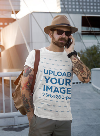 T-Shirt Mockup of a Bearded Man with Tattooed Arms Using His Phone