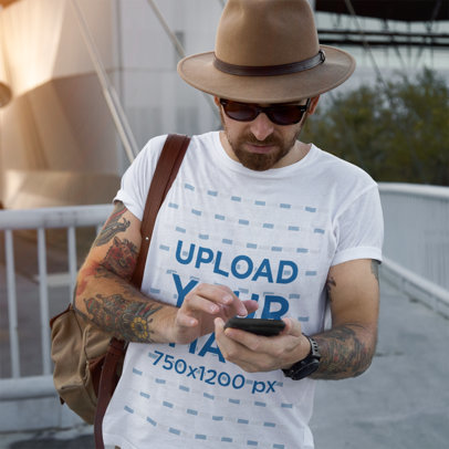 T-Shirt Mockup Featuring a Man With Tattoos Checking His Phone