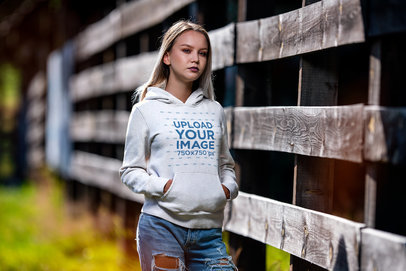 Hoodie Mockup Featuring a Serious Woman Posing Near a Wooden Fence