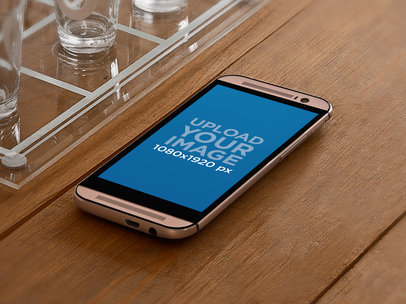 Mockup of an Android Placed on a Wooden Table With Some Glasses