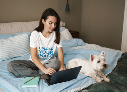 Round-Neck T-Shirt Mockup Featuring a Woman Using Her Laptop on Her Bed with Her Dog