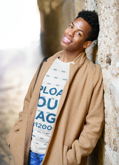 T-Shirt Mockup of a Happy Young Man in a Coat Leaning Against a Wall
