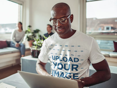 Basic Tee Mockup of a Man with Glasses Working On His Computer