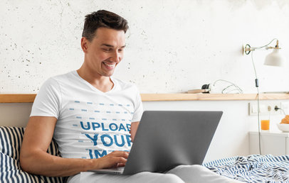V-Neck Tee Mockup of a Happy Man Using His Laptop in Bed