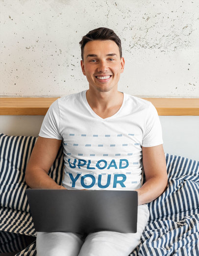 V-Neck Tee Mockup of a Happy Man on His Bed Using His Laptop