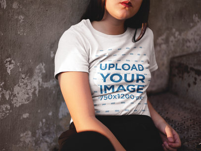 Woman Sitting Down Against a Concrete Wall While Wearing a T-Shirt Mockup