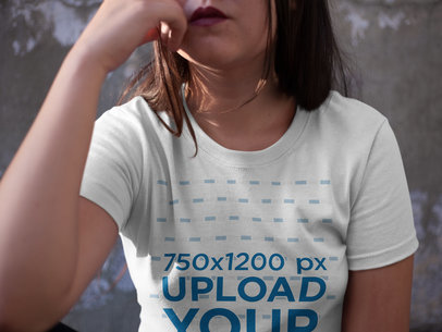 Bored Woman Wearing a T-Shirt Mockup While Sitting Against a Concrete Wall