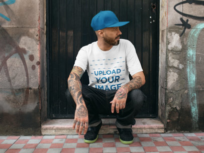 Mockup of a Tattooed Man Looking Aside While Wearing a T-Shirt Mockup and a Hat