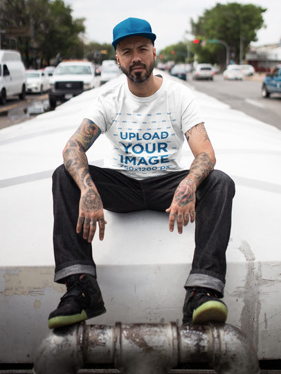 Mockup of a Middle Aged Tattooed Man Wearing a Round Neck Tee Mockup While Sitting Down