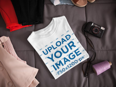 Folded T-Shirt Mockup Lying Next to a Camera and Clothes on a Bed a16941