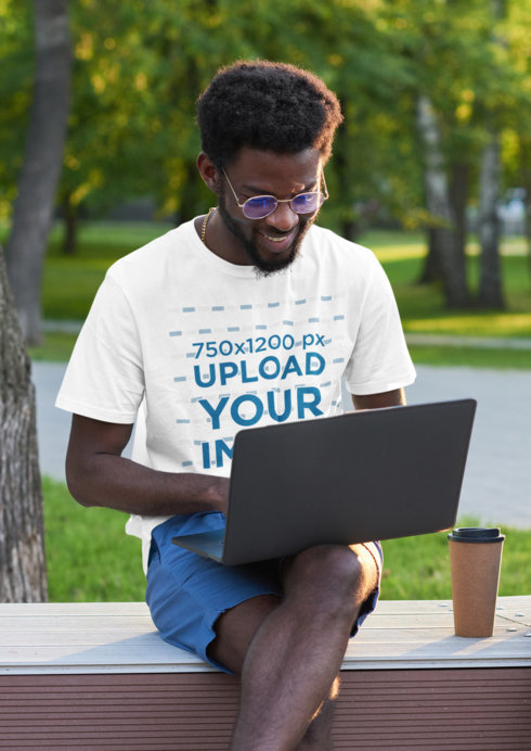 T-Shirt Mockup Featuring a Smiling Bearded Man Working on a Laptop