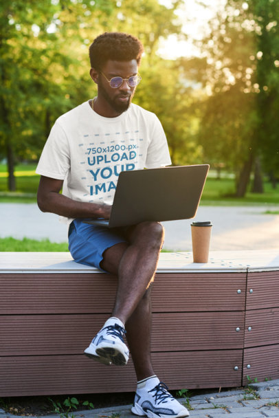Round-Neck T-Shirt Mockup of a Man Working on His Laptop in a Park