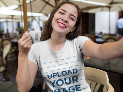 Selfie Mockup of a Smiling Woman Wearing a T-Shirt While Drinking a Coffee
