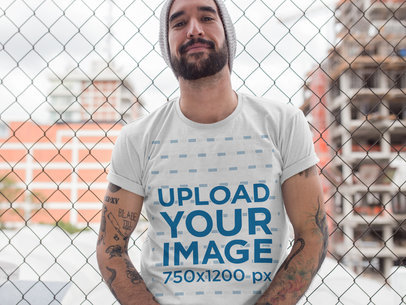 Hipster Middle Aged Man Wearing a Round Neck Tee Mockup While Lying Against a Fence
