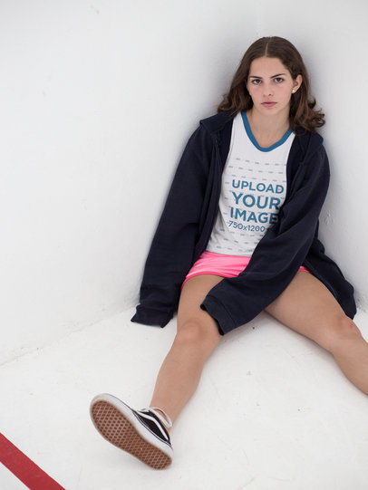 Pretty Woman Wearing a Ringer T-Shirt Mockup While Sitting Against a Corner