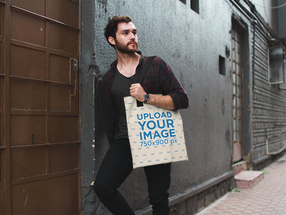 Attractive Man Carrying a Tote Bag Mockup While Against a Wall in an Alley a17090