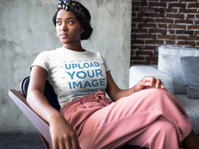 Mockup of a Woman Sitting by the Window at a Living Room Wearing a T-Shirt