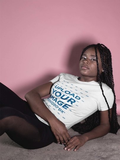 Woman with Locs Wearing a Round Neck Tee Mockup While Lying Near a Pink Wall