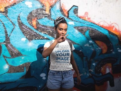 Woman Wearing a Tee Mockup While Making a Horns Sign Against a Graffiti Wall
