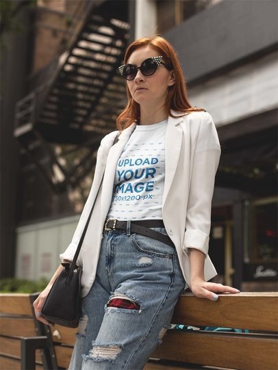 Fashion Woman Wearing a Tshirt Mockup and a White Jacket While Lying Against a Bench